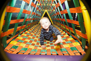 A child crawling on a colorful net bridge in a play area.